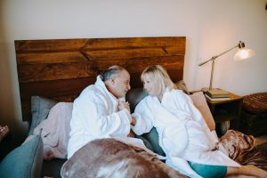 A happy senior couple in white robes smiling and relaxing in bed, portraying warmth and intimacy.