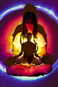 A woman meditates in a colorful aura, promoting mindfulness and spirituality.